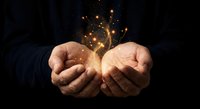 Cupped hands holding glowing golden light particles and sparks against dark background, symbolizing hope, magic, energy and spiritual power.