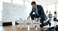 Professional businessman assembling puzzle pieces labeled sales, business integration, and operations in modern conference room during strategic meeting.