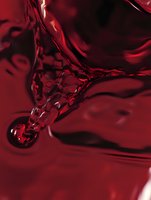 Deep red liquid forms an abstract droplet shape with rippling surface tension, creating dramatic shadows and highlights in macro photography composition.