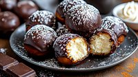 Homemade coconut balls coated in dark chocolate and sprinkled with shredded coconut on gray plate, one cut in half showing creamy white filling. Sweet dessert treat.