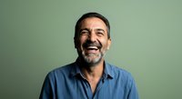 Middle-aged man with dark hair and beard wearing light blue shirt, smiling warmly against soft green background. Portrait suitable for business, corporate, lifestyle, and professional website use.