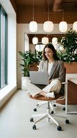 Young professional woman working on laptop in modern office space with pendant lights and plants for remote work and business productivity.