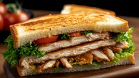 Grilled sandwich with sliced turkey, fresh lettuce and tomato on toasted bread served on wooden board for lunch menu and restaurant advertising.