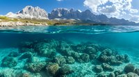 Split view of mountain landscape and underwater coral reef scene with crystal clear turquoise water, rocky peaks and white clouds in summer sky.