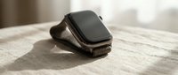 Modern black smartwatch with leather strap on wooden surface in natural sunlight for technology and lifestyle concepts.
