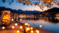 Romantic evening cityscape with glowing string lights and mountain silhouettes reflected in calm water. Blurred bokeh lights create dreamy atmosphere at twilight.