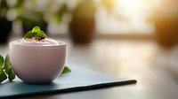 Creamy pink smoothie bowl garnished with fresh mint leaves and seeds on dark surface against blurred warm background, healthy breakfast concept.