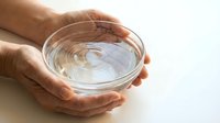 Adult hands holding clear glass bowl with swirling water, studio shot on white background for wellness, hydration, and health-related projects.