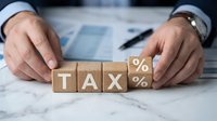 Businessman arranging wooden blocks spelling tax with percentage symbols on marble desk with financial documents and pen for accounting and finance concepts.