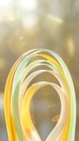 Abstract curved ribbons in soft yellow and green tones creating flowing wave motion against warm blurred bokeh background for modern design projects.