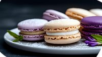 Colorful French macarons in beige and purple shades arranged on white plate with mint leaves and purple flower petals against dark background, macro food photography.