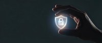 Silhouetted hand holding glowing digital security shield with padlock icon on dark background, representing cybersecurity, data protection, and network safety for technology concepts.
