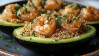 Grilled shrimp served on avocado halves with quinoa and fresh herbs, close up view of gourmet appetizer on rustic plate, selective focus on seafood.