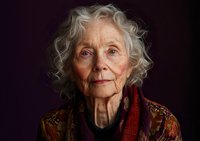 Senior Caucasian woman with silver curly hair wearing colorful knitted sweater against dark background, gentle smile and wise expression showing natural aging beauty.