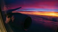 Airplane wing and engine silhouetted against dramatic sunset sky with vibrant pink, orange, and purple clouds during flight. Perfect for travel and aviation content.
