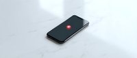 Black smartphone with red notification dot on white marble surface showing missed call or message alert for mobile communication concepts.