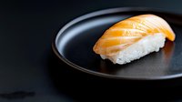 Fresh salmon nigiri sushi piece on black ceramic plate against dark background, traditional Japanese cuisine with raw fish and white rice.
