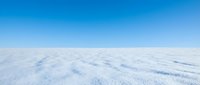 Aerial view of endless snow-covered landscape stretching to horizon under clear blue sky, suitable for winter backgrounds and nature projects.