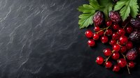 Fresh red currants and cherries with green leaves arranged on dark slate stone background for culinary and food photography projects.