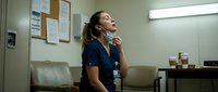 Exhausted female healthcare worker in scrubs taking break in hospital break room after long shift looking up with tired expression.
