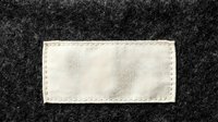 Blank white fabric label sewn onto dark gray wool textile with visible stitching for branding and product identification purposes.