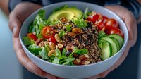 Fresh quinoa bowl with avocado, cherry tomatoes, cucumber slices, mixed greens and roasted nuts served in white ceramic bowl, healthy lunch concept.