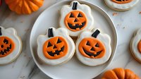 Halloween pumpkin sugar cookies with orange royal icing and black jack-o-lantern faces on white plate, perfect for autumn baking and seasonal treats.