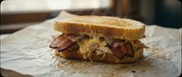 Crispy bacon sandwich with melted cheese on toasted bread served on parchment paper. Classic comfort food for breakfast, lunch or snack time dining.