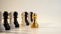 Golden chess pawn standing out from crowd of black and white pawns on wooden surface symbolizing leadership and uniqueness in business strategy.