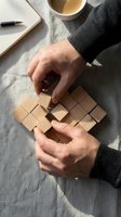 Male hands solving wooden cube puzzle on linen surface with coffee and notebook, problem-solving and strategic thinking concept for business planning.