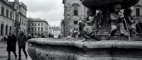 Historic fountain with ornate sculptures in European city square captured in artistic black and white photography showcasing classical architecture and urban heritage.