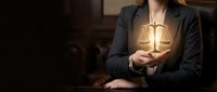 Professional female lawyer holding glowing scales of justice symbol in dark office representing legal services and law firm consultation.