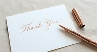 Elegant thank you card with rose gold calligraphy on white paper beside luxury copper pen on textured background for gratitude expression.