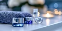 Luxury spa composition with blue cosmetic jars, soft towel and glowing candles on white surface creating tranquil atmosphere for wellness and beauty treatments.