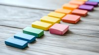Colorful sticky notes arranged in rainbow sequence on rustic wooden background, creating minimal composition for organization and planning purposes.