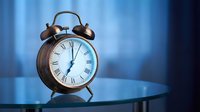 Vintage copper alarm clock showing midnight on glass table with dramatic blue lighting creating atmospheric mood for time management concepts.