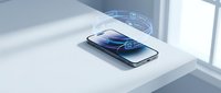 Modern smartphone with wireless charging technology displaying blue energy waves on minimalist white desk surface in bright contemporary office setting.