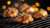 Grilled chicken thighs with honey glaze and sesame seeds on barbecue grate, golden bokeh lights in background creating festive mood for outdoor cooking.