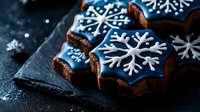 Festive chocolate cookies decorated with blue icing and white snowflake patterns on dark slate background, perfect for winter holiday celebrations.