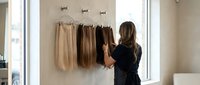 Professional hairstylist examining hair extension samples in modern salon. Woman selecting from blonde to brunette color swatches for client consultation.