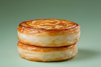 Flaky golden puff pastry rounds stacked together showing delicate layers and buttery texture on mint green background. Freshly baked French pastry closeup.