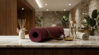 Burgundy yoga mat rolled on wooden table with aromatherapy diffuser and towels in modern wellness studio interior for meditation and fitness practice.