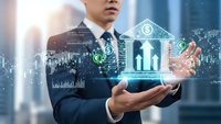 Businessman holding digital holographic house icon with family silhouette and financial data charts representing real estate investment technology.