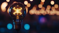 Glowing vintage filament light bulb with warm illumination against blurred bokeh background, creating atmospheric mood for creative and innovation concepts.