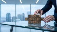 Professional businessman arranging wooden letter blocks spelling SMALL BUSINESS GRANT on glass table in modern office with city skyline view through windows.