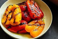 Grilled red and yellow bell peppers with charred grill marks served in ceramic bowl, marinated in olive oil, showcasing vibrant colors and smoky texture for Mediterranean cuisine.