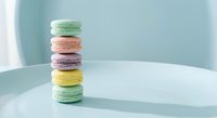 Colorful French macarons stacked on mint green plate against soft blue background. Delicate pastry tower with pastel colors for bakery and dessert concepts.