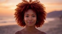 Young African American woman with natural curly afro hair at golden hour sunset beach portrait with warm lighting and soft focus background.