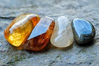 Polished healing crystals in amber, orange, clear quartz and labradorite arranged on natural stone surface showing mineral texture and translucent properties.