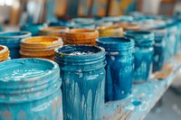 Colorful paint jars with dripping blue and orange acrylic colors arranged in row on shelf, selective focus on turquoise paint container showing artistic texture.